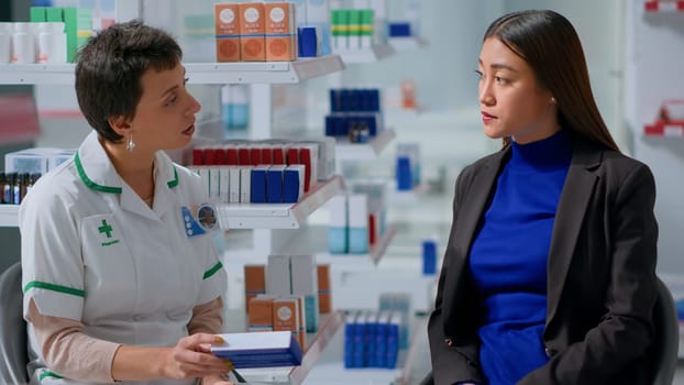 Experienced pharmacist in drugstore with patient after finishing annual checkup, suggesting her medical products to treat disease symptoms. Asian woman receiving treatment from healthcare practitioner