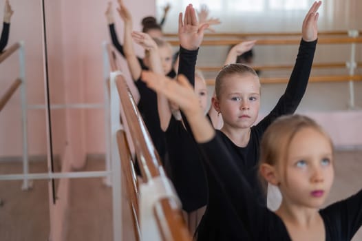 Cute little girls in black swimsuits and tutu do ballet at the barre