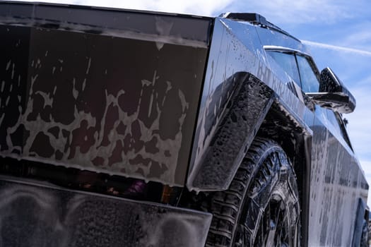 Denver, Colorado, USA-May 5, 2024-Close-up image of a Tesla Cybertruck being washed, showcasing the vehicle angular design and rugged tires. Water and soap suds cover the metallic surface, highlighting the unique texture and design elements of the electric truck.