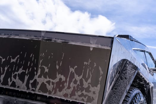 Denver, Colorado, USA-May 5, 2024-Close-up image of a Tesla Cybertruck being washed, showcasing the vehicle angular design and rugged tires. Water and soap suds cover the metallic surface, highlighting the unique texture and design elements of the electric truck.