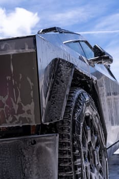 Denver, Colorado, USA-May 5, 2024-Close-up image of a Tesla Cybertruck being washed, showcasing the vehicle angular design and rugged tires. Water and soap suds cover the metallic surface, highlighting the unique texture and design elements of the electric truck.