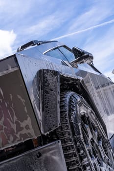 Denver, Colorado, USA-May 5, 2024-Close-up image of a Tesla Cybertruck being washed, showcasing the vehicle angular design and rugged tires. Water and soap suds cover the metallic surface, highlighting the unique texture and design elements of the electric truck.