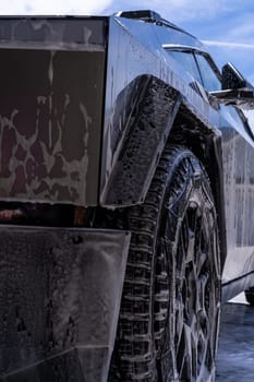 Denver, Colorado, USA-May 5, 2024-Close-up image of a Tesla Cybertruck being washed, showcasing the vehicle angular design and rugged tires. Water and soap suds cover the metallic surface, highlighting the unique texture and design elements of the electric truck.