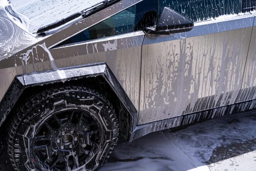 Denver, Colorado, USA-May 5, 2024-Close-up image of a Tesla Cybertruck being washed, showcasing the vehicle angular design and rugged tires. Water and soap suds cover the metallic surface, highlighting the unique texture and design elements of the electric truck.
