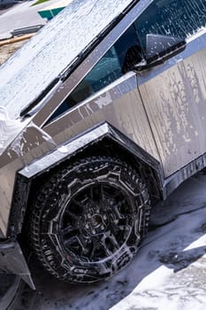 Denver, Colorado, USA-May 5, 2024-Close-up image of a Tesla Cybertruck being washed, showcasing the vehicle angular design and rugged tires. Water and soap suds cover the metallic surface, highlighting the unique texture and design elements of the electric truck.