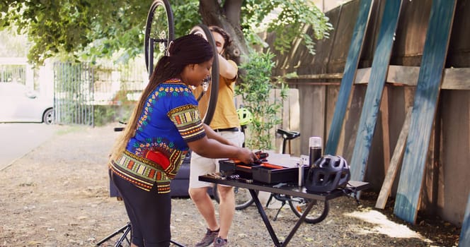 Active african american female consulting with healthy caucasian male on suitable work tool to use for realigning bike pedals. Multiethnic couple talking and servicing modern bicycle in yard.