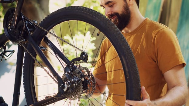 Energetic fit caucasian man outside repairing and maintaining bicycle components using specific tools. Male cyclist carefully examining and fixing damaged bike with great enthusiasm.