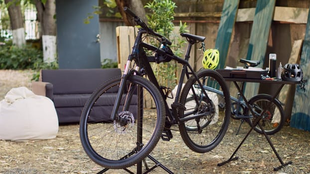 View of bicycle on repair-stand surrounded by specialized equipment outside for maintenance and repair. Modern damaged bikes for repairing and adjusting in home yard by its owners.