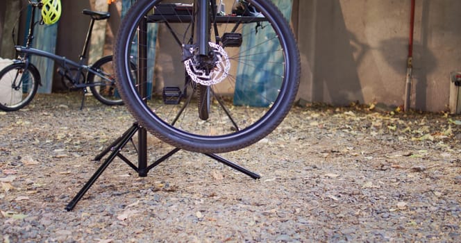 Detailed view of damaged bike mounted on repair-stand ready for repair with assortment of tools outdoor. Annual summer upkeeping and servicing of modern bicycle in home yard.