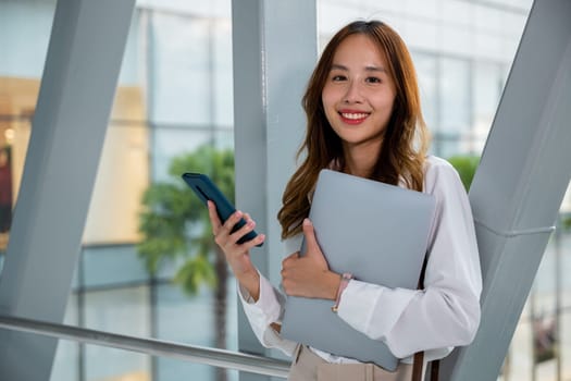 Busy female entrepreneur in airport with laptop and cell phone. Efficient multitasking to manage business remotely. Stay connected and productive while traveling