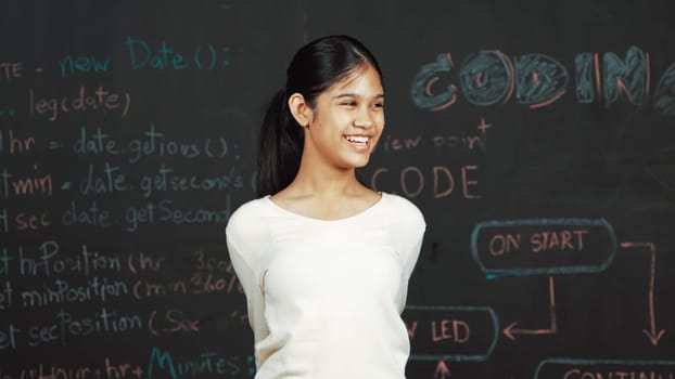 Young student celebrate her successful plan while raise her arm. Happy teenager looking at camera while standing at blackboard with engineering code and prompt written in STEM class. Edification.