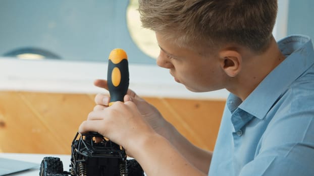 Close up of young student tighten the nut by using screwdriver. Caucasian teenager repairing or fixing car model while inspect robotic machine construction at STEM technology class. Edification.