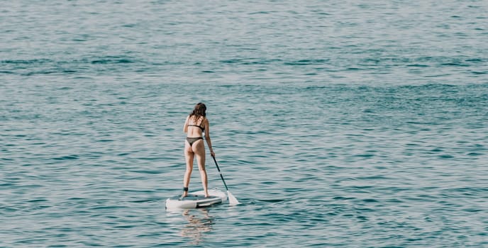 Sea woman sup. A happy positive woman in hat with family relaxing in sea, aerial back view of family on SUP board floating on calm water. Active lifestyle at sea. Summer vacation. Slow motion