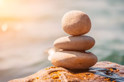 Balanced Pebbles Pyramid on the Beach on Sunny Day and Clear Sky at Sunset. Blue Sea on Background Selective focus, zen stones on sea beach, meditation, spa, harmony, calm, balance concept.