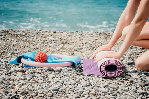 Young woman with long hair in white swimsuit and boho style braclets practicing outdoors on yoga mat by the sea on a sunset. Women's yoga fitness routine. Healthy lifestyle, harmony and meditation