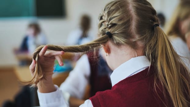 A girl touches a braid of her hair during class
