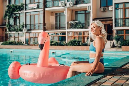 Happy woman in bikini sitting near swimming pool, summer vacation