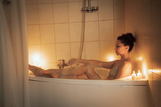 A woman is sitting in a bathtub with candles lit around her. Scene is relaxing and calming