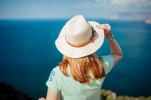A woman wearing a straw hat is standing on a beach looking out at the ocean. The hat is brown and white, and the woman's hair is long. The scene is peaceful and relaxing