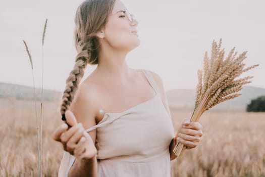 A woman is holding a bunch of wheat in her arms. The wheat is dry and brown, and the woman is wearing a white dress. The scene is set in a field, and the woman is posing for a photo