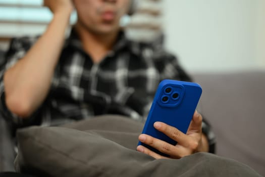 Young man listening to music with wireless headphones using mobile phone at home.