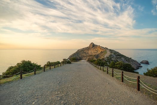 A rocky beach with a long road leading to a cliff. The road is lined with wooden posts and the sky is cloudy