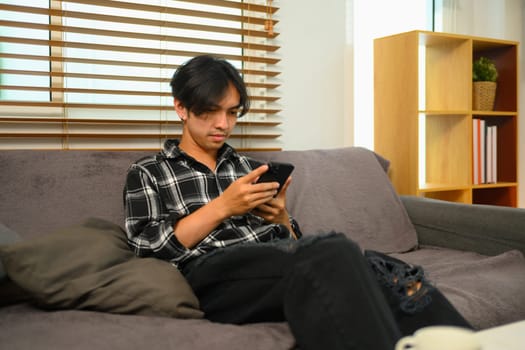 Young man freelancer resting on couch and reading message on mobile phone.