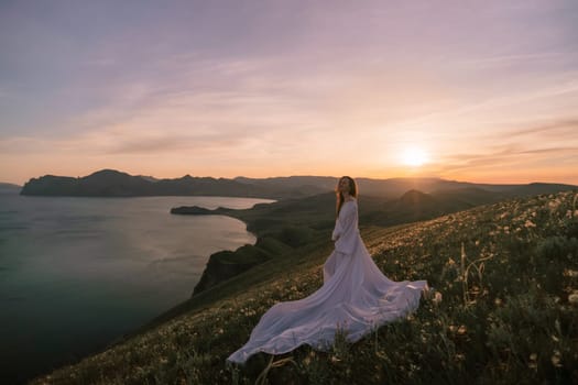 A woman in a white dress stands on a hill overlooking a body of water. The sky is a mix of blue and pink, and the sun is setting in the distance. The scene is serene and peaceful