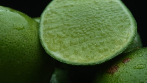 Slices of lime are meticulously arranged in a pile, set against a black background. Each lime slice is captured in stunning detail, its vibrant green hue and enticing texture. Close up. Comestible.