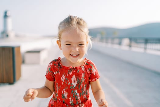 Little laughing girl stands on the sunny embankment. High quality photo