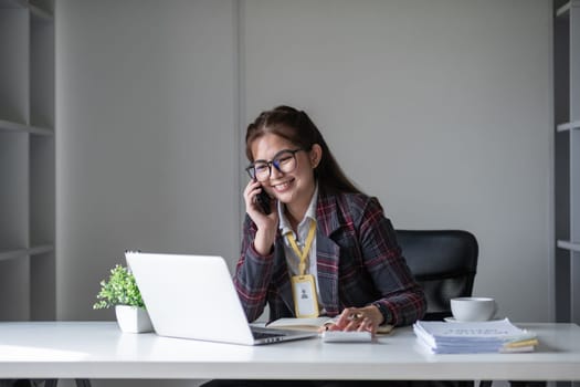 Beautiful accountant talking on the phone and calculating financial figures and calculating taxes for the company..