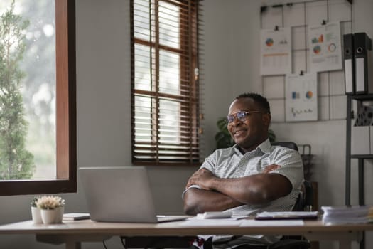 African American businessman working on paperwork, searching for information with laptop at home office.