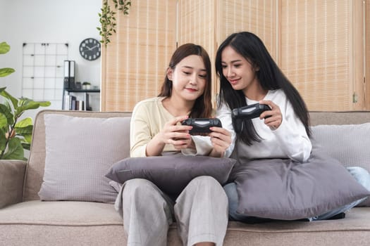 Young LGBT woman, lesbian couple, sitting on the sofa, playing games on a joystick together, having fun..
