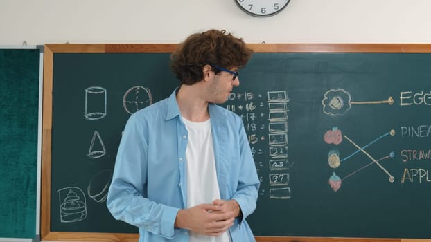 Caucasian smart teacher teach while student standing at blackboard and listening instructor at classroom. Professional diverse children looking at teacher pointing at blackboard. Education. Pedagogy.