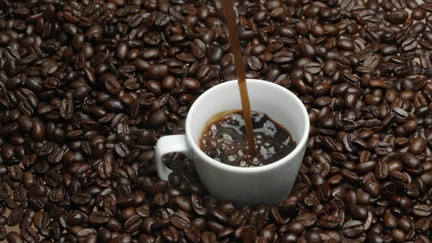 Freshly espresso was poured in white cup with pile of coffee bean. Pouring black coffee in the cup with brown background and seed scattering around on wooden table. Close up. Top view. Comestible.