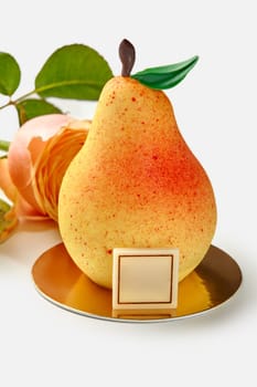 Appetizing pear-shaped mousse dessert made with fruit confit decorated with colored chocolate leaf and stem on golden serving cardboard on white background with fresh rose