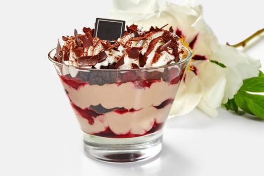 Glass of tempting layered trifle with chocolate sponge cake, sweet ripe cherries and whipped cream topped with chocolate shavings and cocoa powder adorned with delicate white peony