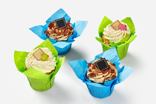 Delicious vanilla and chocolate cupcakes topped with swirls of whipped cream with decorations presented in blue and green paper wrappers on white background