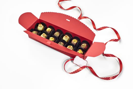 Exquisite chocolate candies decorated with hazelnuts, caramel crumbs and golden pearls, packaged in red gift box with dotted ribbon and signature label, perfect for special occasions