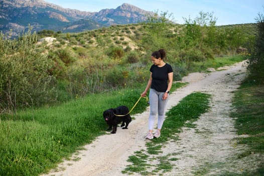 Full size shot of a happy woman smiling looking away, walking her dog in mountains outdoors. People, nature and playing pets concept. Front view