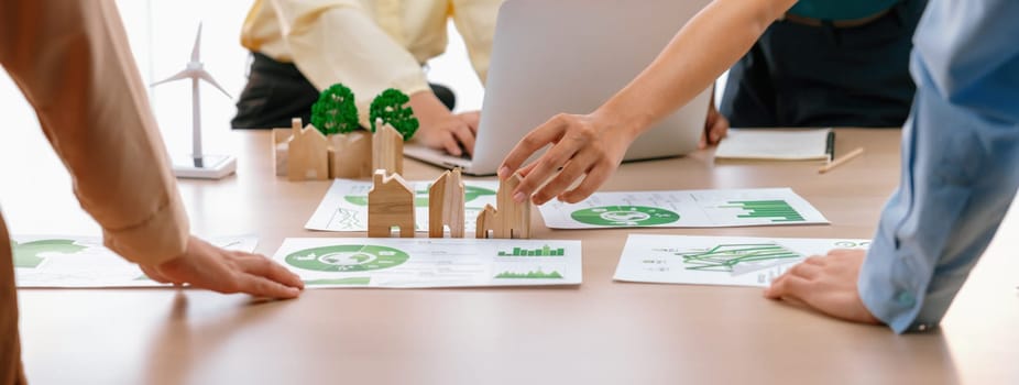 Wooden block represented green city and wind mill represented renewable energy was placed at center of green business meeting table with environmental document. Green business concept. Delineation.