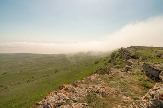 A foggy mountain top with a clear blue sky in the background. The sky is filled with clouds, giving the scene a serene and peaceful atmosphere