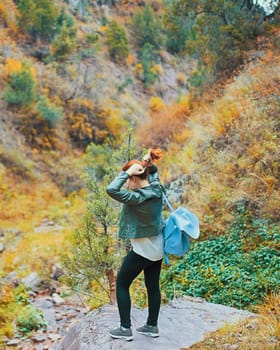 Female hiker walking in mountains forest. A woman with a backpack is standing on a big stone in the mountains in the forest.