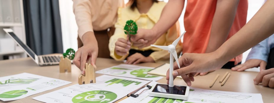 Windmill model represented using renewable energy placed during presenting green business on table with wooden block and environmental document scatter around. Closeup. Delineation.