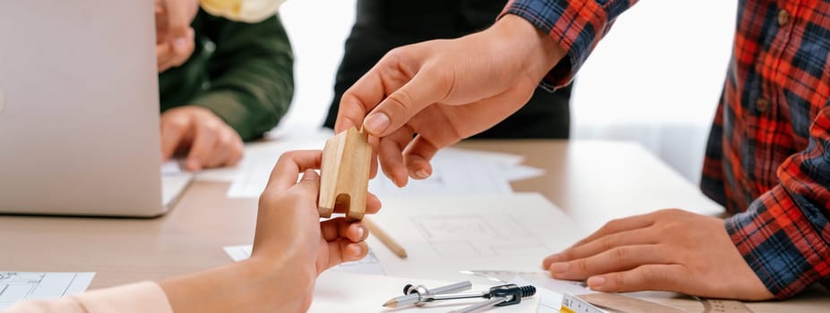 Professional architect team discussion about architectural project on meeting table with blueprint and wooden block scatter around at modern office. Closeup. Focus on hand. Delineation.