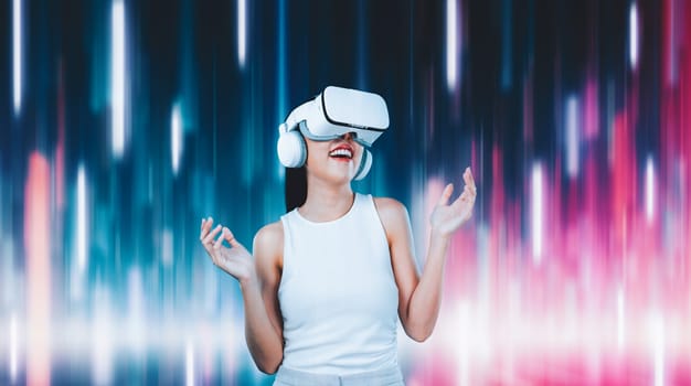 Female standing and wearing white VR headset and white sleeveless connect metaverse, future technology creating cyberspace community. She enjoy look fantasy abstract light around her. Hallucination.