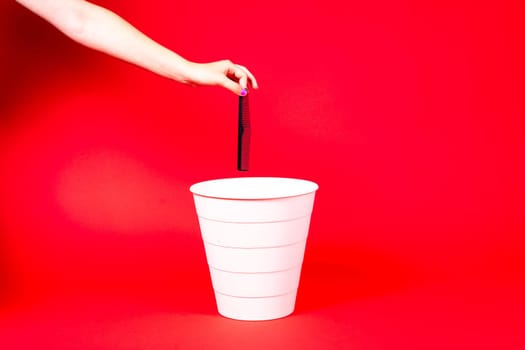 Hand throws plastic comb into trash bin with package on a red background