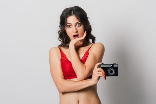 Beautiful female with pretty smile in red lingerie pinup style holding photo camera, isolated on white