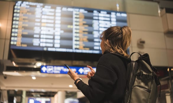 Young Asian woman in international airport looking at flight information board, checking her flight.