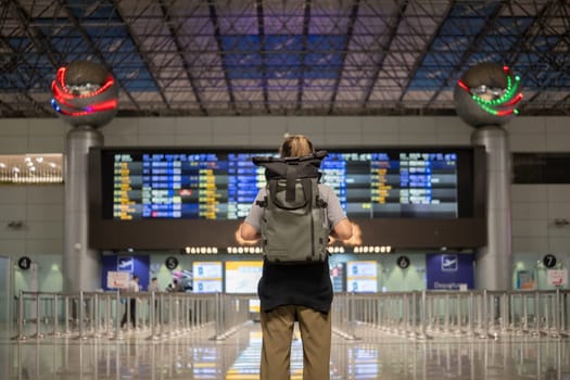 Young Asian woman in international airport looking at flight information board, checking her flight.